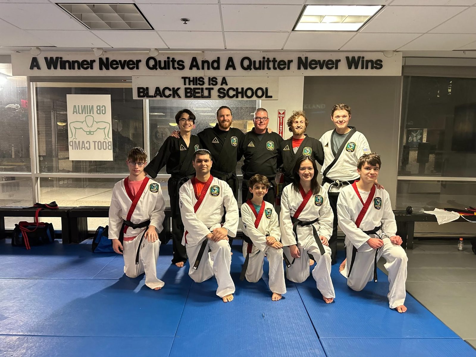 Giroux Bros Martial Arts black belts and students under the "A Winner Never Quits" banner in the Newtonville dojo